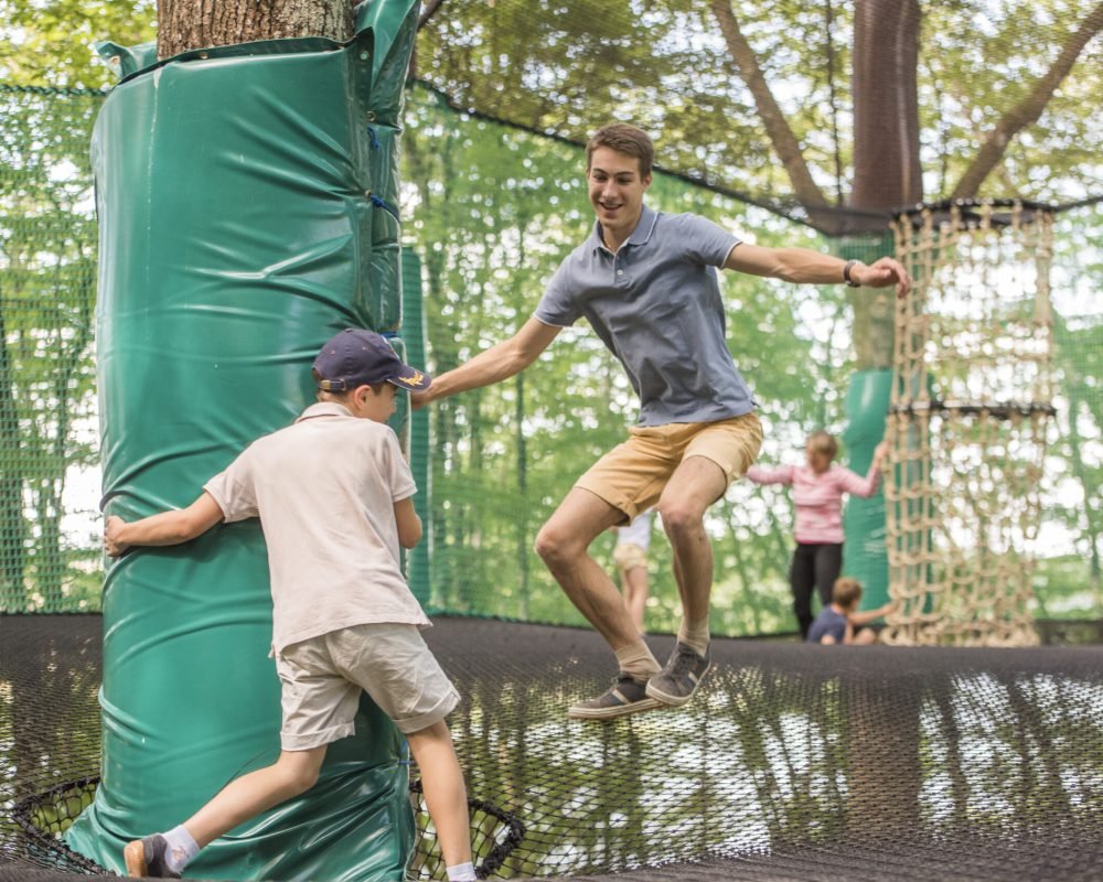 Ados et enfants sautant sur des Arbofilets géants suspendus entre les arbres, installation Arboricorde